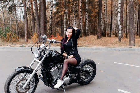 the beautiful brunette in a dress on a motorcycle in the parkの写真素材