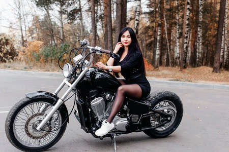 the beautiful brunette in a dress on a motorcycle in the parkの写真素材