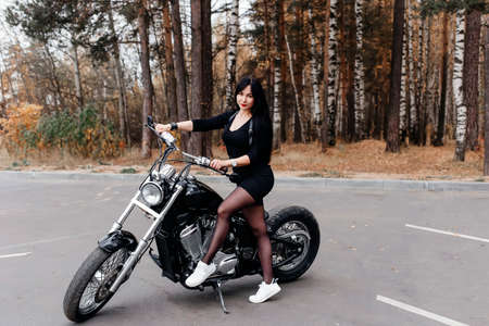 the beautiful brunette in a dress on a motorcycle in the parkの写真素材