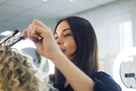 the master makes a hairstyle for a girl, beautiful curlsの写真素材