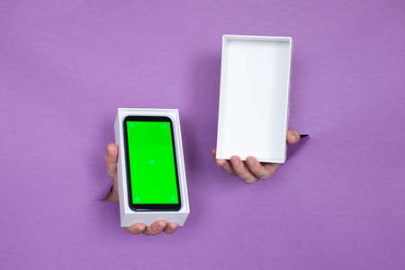 a new smartphone with a green screen in a package on a purple background, a girl holds in her hands,...