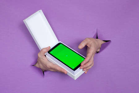 a new smartphone with a green screen in a package on a purple background, a girl holds in her hands, holes in the background.の写真素材