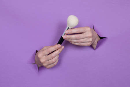 professional makeup brushes in your hands, on a purple background, holes in the background. Space for text.の写真素材