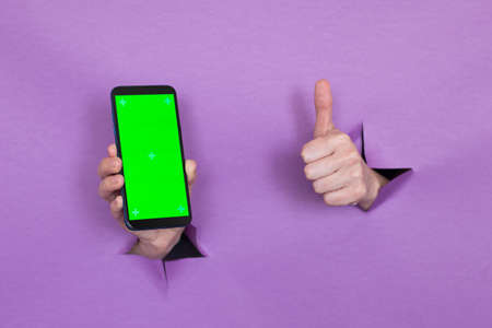 phone with green screen in hand on purple background, hand gesture, through the background hand slot.の写真素材