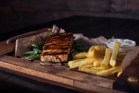 salmon fillet steak with french fries on a wooden tray, beautiful serving, dark background.の写真素材