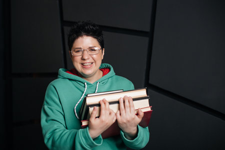 brunette girl with short hair wearing glasses with books, on a black background.の写真素材