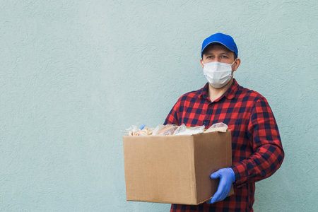 male volunteer wearing a protective mask with a box of groceries, charity.