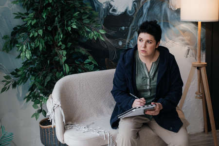 girl with short hair, writes in a notebook and makes phone calls, remote work from home.