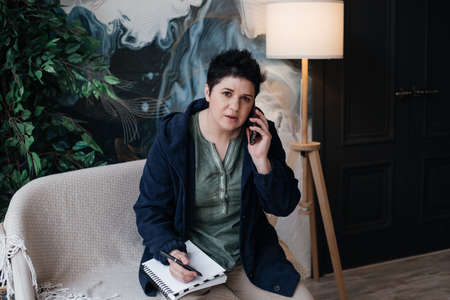 girl with short hair, writes in a notebook and makes phone calls, remote work from home.