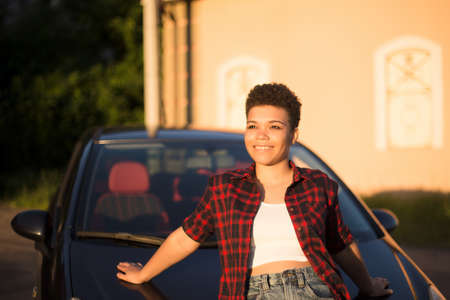 happy and beautiful african american woman with short hair near the car, lifestyle.