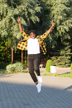 a happy African American woman in the park makes a jump in the summer.