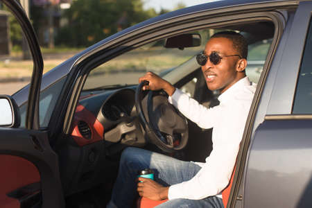happy african american driving a car with coffee, in the summer.