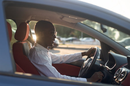 happy african american driving a car with a phone, in the summer.の写真素材