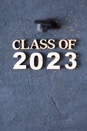 Class of 2023 concept. Wooden number 2023 with golden tinsel and graduated cap on dark background.