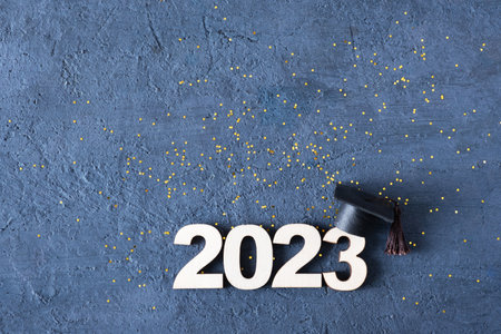 Class of 2023 concept. Wooden number 2023 with graduate hat on dark concrete background with tinsel top view.の写真素材