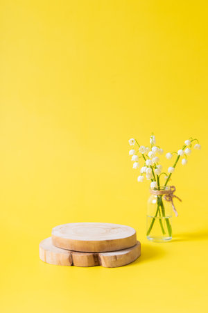 Wooden podium or pedestal with lilies of the valley bouquet in a mini jar on a yellow background.の写真素材