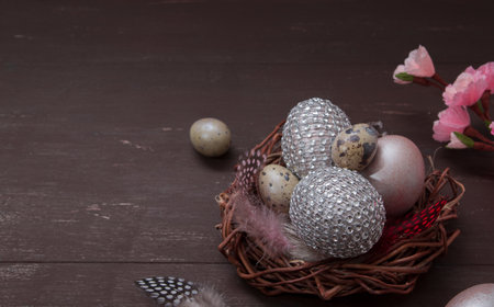 Creative Easter still life with a nest with eggs in rhinestones with a bow and a flowering branch in...