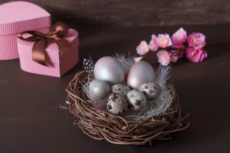 Easter nest with eggs on brown bakcground with pink blossom flowers and gift boxes.