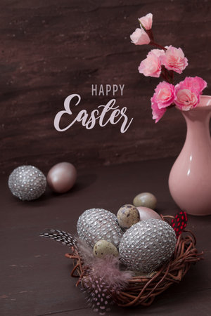 Happy Easter greeting text with nest and eggs on brown bakcground with pink blossom flowers low key still lifeの写真素材