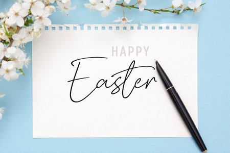 Happy Easter inscription on paper sheet with blooming branch on color bakcgroundの写真素材