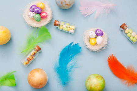 Top view easter eggs in nest and glass bottles and colorful feathers on a blue backgroundの写真素材