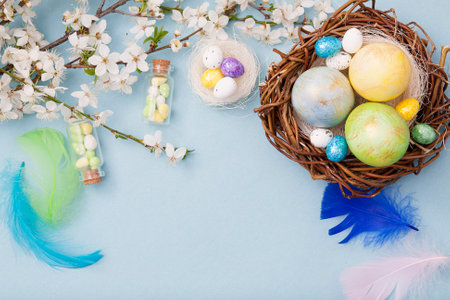 Top view easter eggs in nest and glass bottles on a blue background with blossom flowers. Copy space...