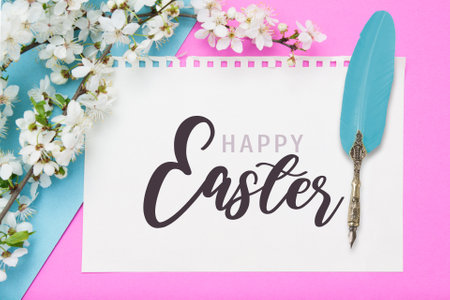Happy Easter inscription on paper sheet with blooming branch on color bakcgroundの写真素材