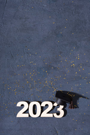 Class of 2023 concept. Wooden number 2023 with graduate statuette on concrete background with tinsel...