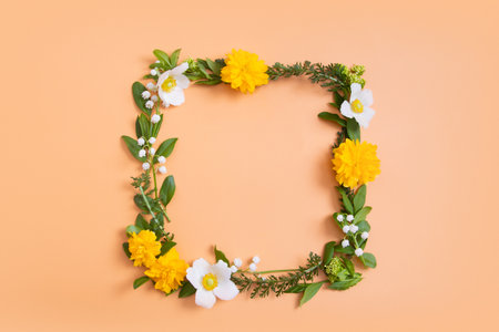 Summer or spring composition on a orange background. Yellow and white flowers and green leaves with a copy space wreath top view. Summer, spring floral concept.の写真素材