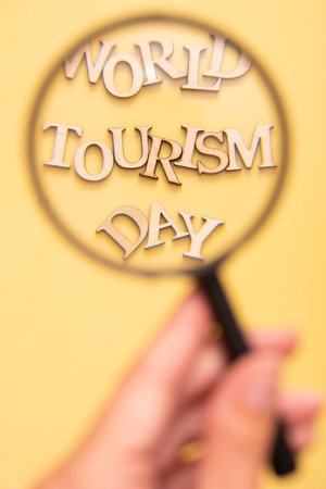 World Tourism Day text from wooden letters on a yellow background through a magnifying glass.の写真素材