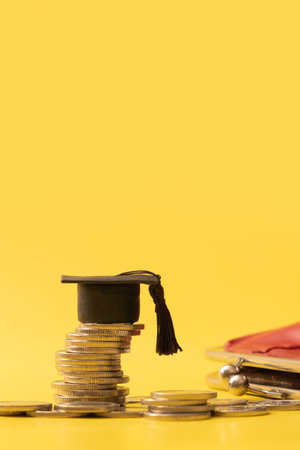 Graduated cap with coins on yellow background. Savings for education concept. vertical photoの写真素材