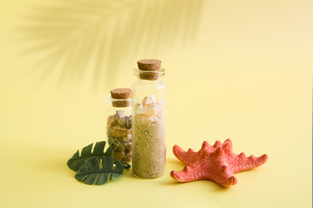 Minimalistic summer idea with mini bottles and small shells, sea star and tropical leaves on yellow background. The creative still life about sea, vacation, travelの写真素材