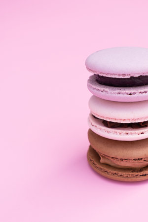 Different colors pastry macarons on a pink background.