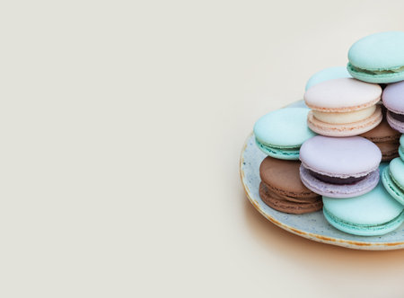 Different pastel colors pastry macarons in plate on a beige background with copy space.