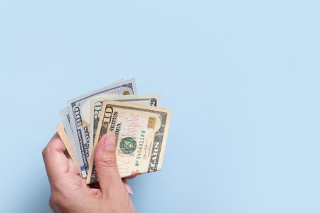 Dollars in female hand on blue background. Minimalistic financial concept.