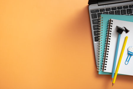Colorful pencils with graduated cap and note on laptop on colored background. copyspace. Children work space top view, flat lay.の写真素材