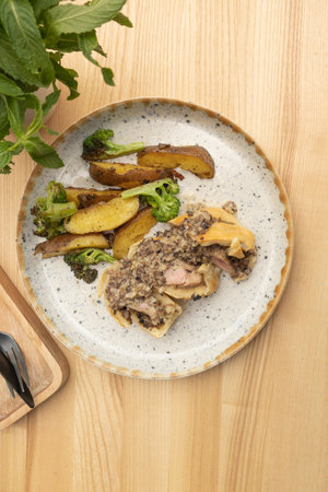 Baked meat in dough with potatoes and broccoli on wooden tableの写真素材