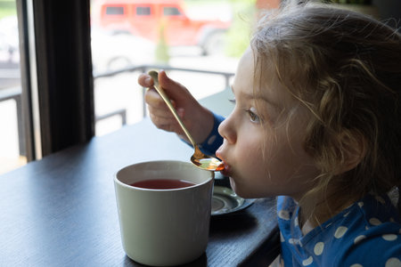 A little girl drinks tea with a teaspoon in a cafe.の写真素材