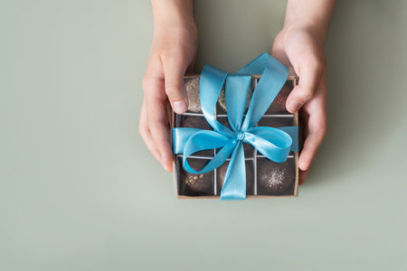 Gift box with chocolate craft candies in boys hands. Sweet gift box.の写真素材
