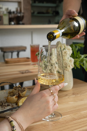 White wine is poured into a glass at a table in a cafe.の写真素材