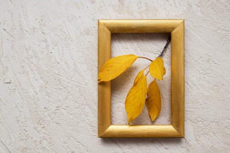 A branch of orange leaves in a gold photo frame on a plaster background. Autumn concept. Copy spaceの写真素材