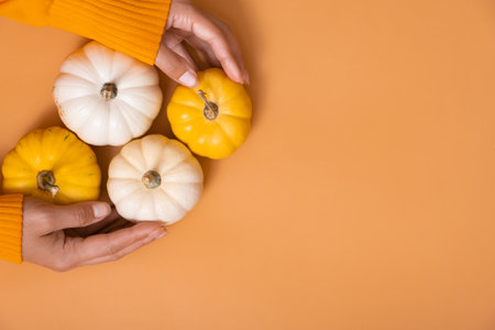 A small decorative pumpkins in a woman's hand in a sweater on an orange background.の写真素材