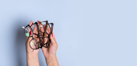 Female hands with eye glasses on a blue banner background. Optical store, vision test, stylish glasses concept.の写真素材