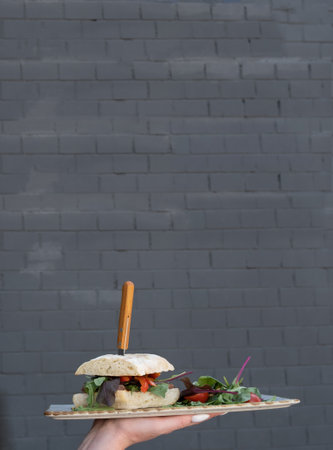 Waitress hand holding a burger with meat on brik wall background.の写真素材