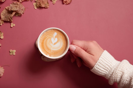 Female hand in sweater holding cup of cocoa on dark pink color background, top view.の写真素材
