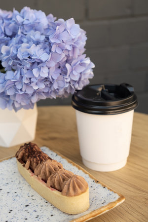 Cake with shortcrust pastry and cream on a wooden cafe table on a background of flowers.