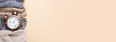 Banner with alarm clock and cozy sweaters with copy space on beige background. Top view.