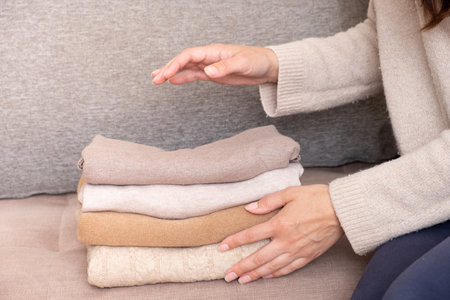Female hands stack cozy knitted sweaters on the sofa. Warm concept.の写真素材