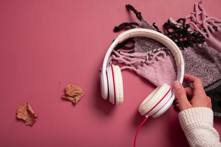 Female hand with headphones and plaid on dark pink color background. Creative music, relax, online concept.の写真素材