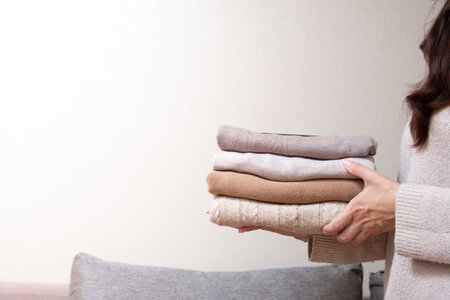 Stack of cozy knitted sweaters in female hands on sofa background. Warm concept.の写真素材